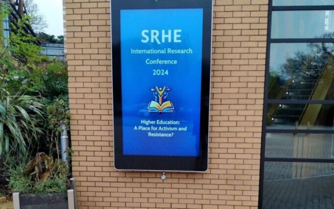 SRHE 2024 backlit conference welcome board on exterior wall of conference centre.