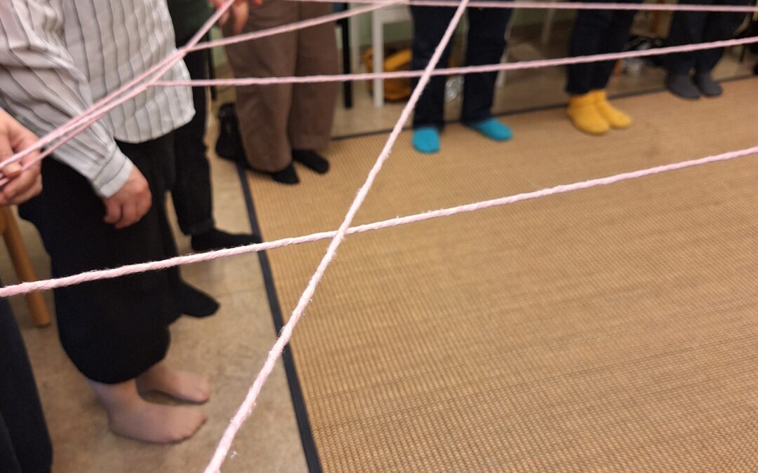 A standing circle of people interconnected by strands of wool