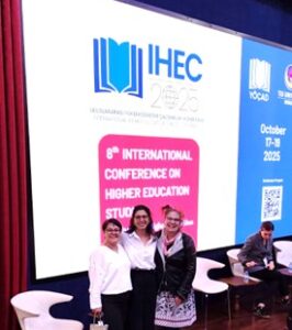 Professor Susanne Maria Weber, Kardelen Cazgir and IHEC colleague at conference on higher education studies. The group of three are standing in front of a large screen with an IHEC slide showing.